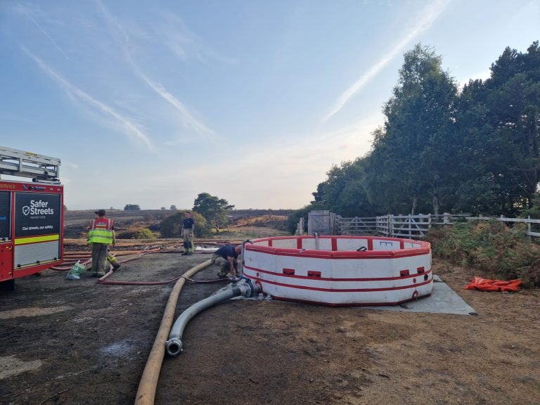 A water dam is set up in the Noew Forest - this looks like a large inflatable paddling pool. It's designed to hold a large amount of water at the incident. Hoses run out from the dam and firefighters are working in the background.